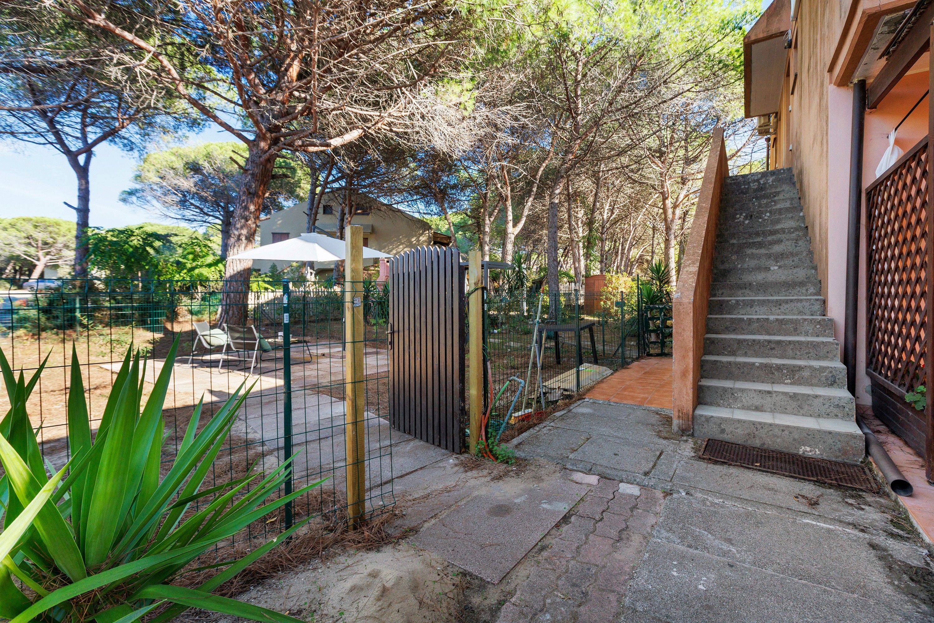 A residential property with a paved driveway, a gated entrance, outdoor seating, and a staircase leading to a building.