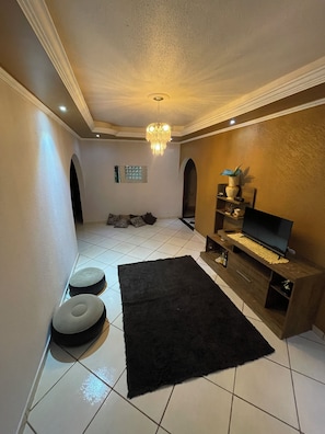 Una sala de estar moderna con un tapete negro, un televisor sobre un mueble de madera y una araña.