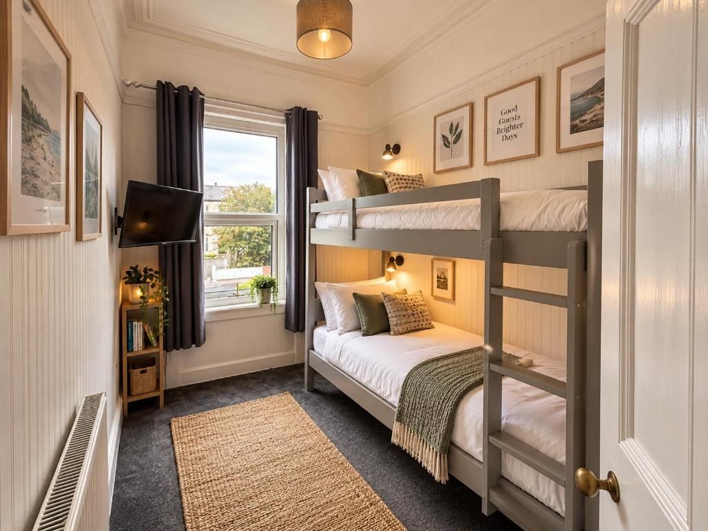 A bedroom with bunk beds, a television, a window with curtains, and framed pictures on the wall.