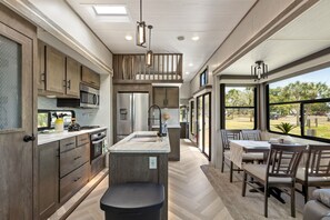A modern kitchen with a central island, built-in appliances, and a dining area with a view. - Marvelous 3-bedroom mobile home with AC and Waterfront Views in Cedar Key (Cedar Key)