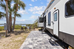 A white RV parked on a paved area with a view of a lake and palm trees. - Marvelous 3-bedroom mobile home with AC and Waterfront Views in Cedar Key (Cedar Key)