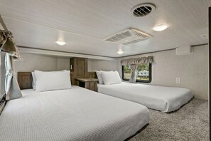 A bedroom with two beds, a small table, and a window with curtains. - Marvelous 3-bedroom mobile home with AC and Waterfront Views in Cedar Key (Cedar Key)