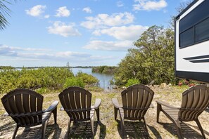 Three Adirondack chairs facing a body of water with a boat parked nearby. - Marvelous 3-bedroom mobile home with AC and Waterfront Views in Cedar Key (Cedar Key)