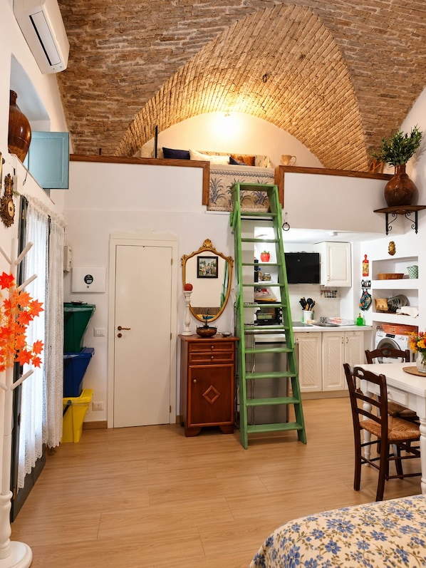 A compact kitchen with a lofted sleeping area, a green ladder, and a dining table.
