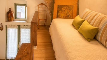 Un dormitori acollidor amb sostre inclinat, una banca de fusta, un llit amb almoadines, una finestra amb cortines i un quadre penjat a la paret.