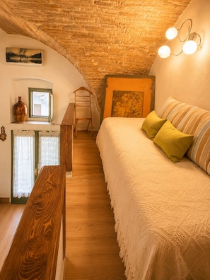 A cozy bedroom with a sloped ceiling, a wooden bench, a bed with pillows, a window with curtains, and a wall-mounted picture.