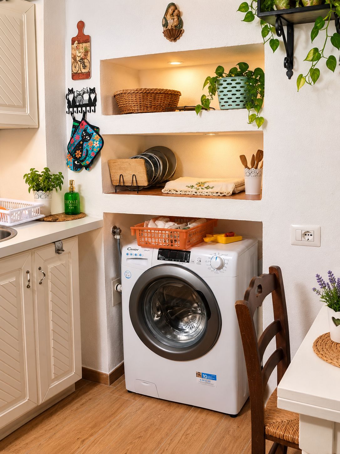 Cocina compacta con lavadora y secadora integradas, repisas con cestas y utensilios de cocina, y un comedor con una silla y una mesa.