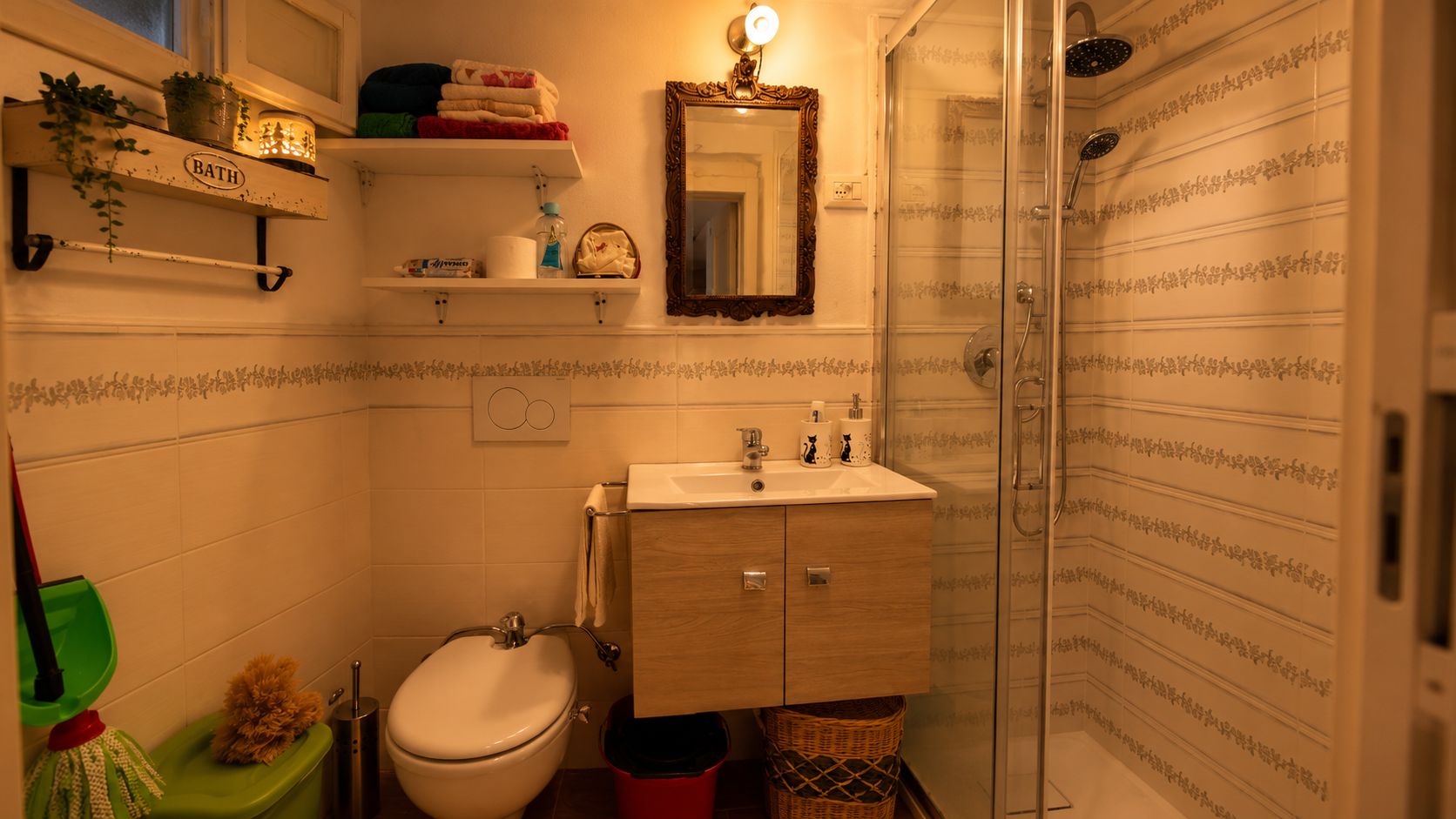 Een badkamer met toilet, wastafel en douche. Boven het toilet zijn planken en boven de wastafel een spiegel.