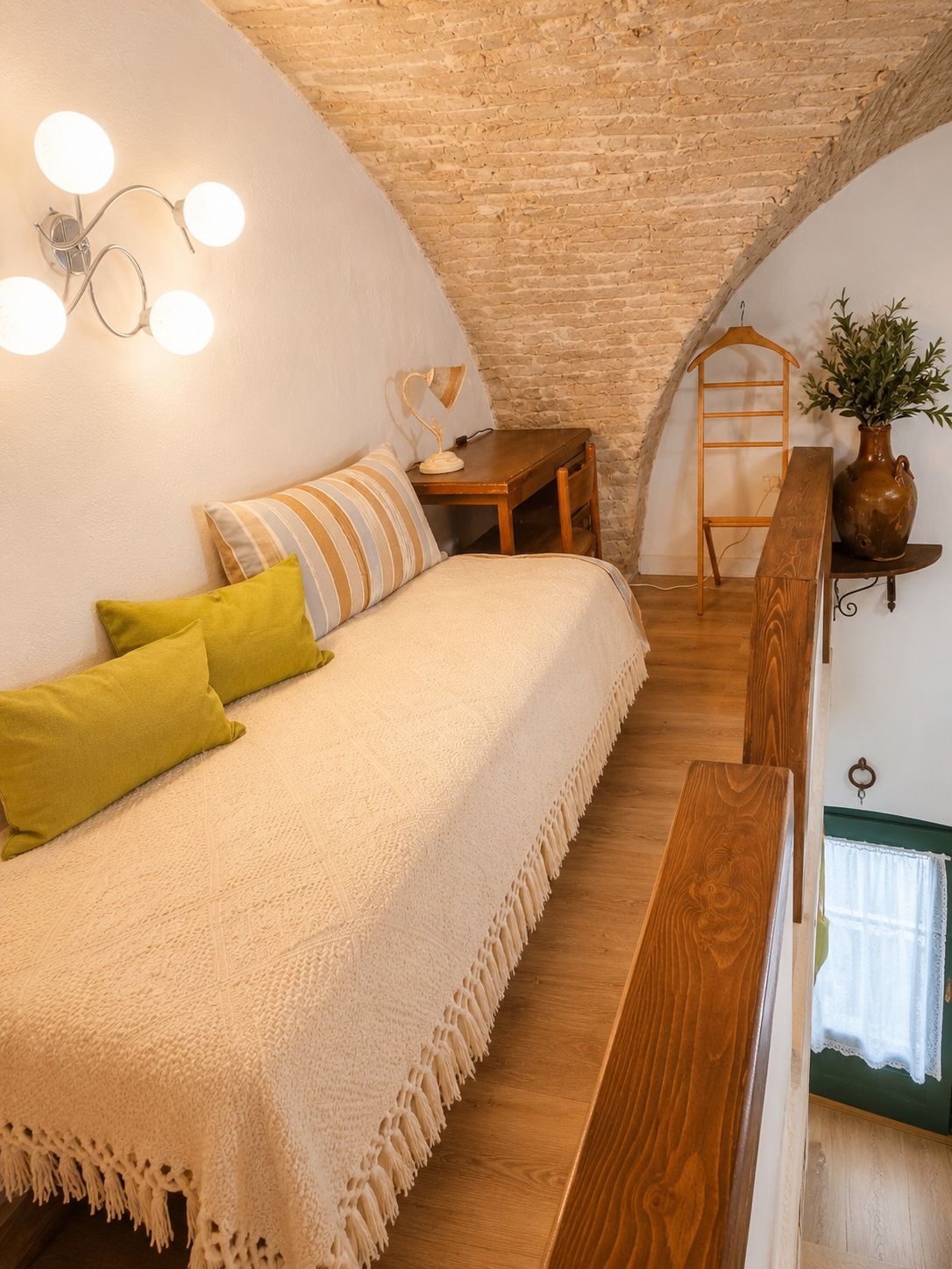 A cozy room with a bed, a wooden bench, a small table, and a hanging plant.