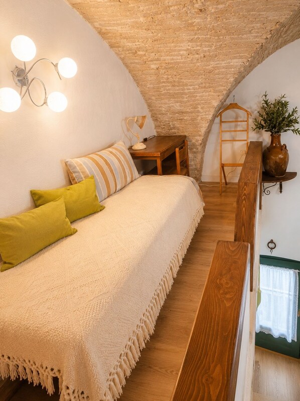 A cozy room with a bed, a wooden bench, a small table, and a hanging plant.