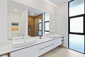 A modern bathroom with two sinks, a large mirror, and a view of the outdoors through a large window.