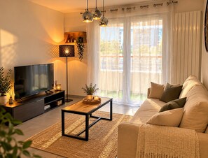 A modern living room with a flat-screen TV, a coffee table, a sofa, and a large window with curtains. - Le Cocon de Saint-Herblain, private parking (Saint-Herblain)