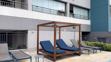 A poolside area with a wooden canopy, lounge chairs, and a small table.