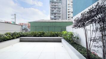 A rooftop terrace with a view of surrounding buildings, a green fence, and some vegetation.