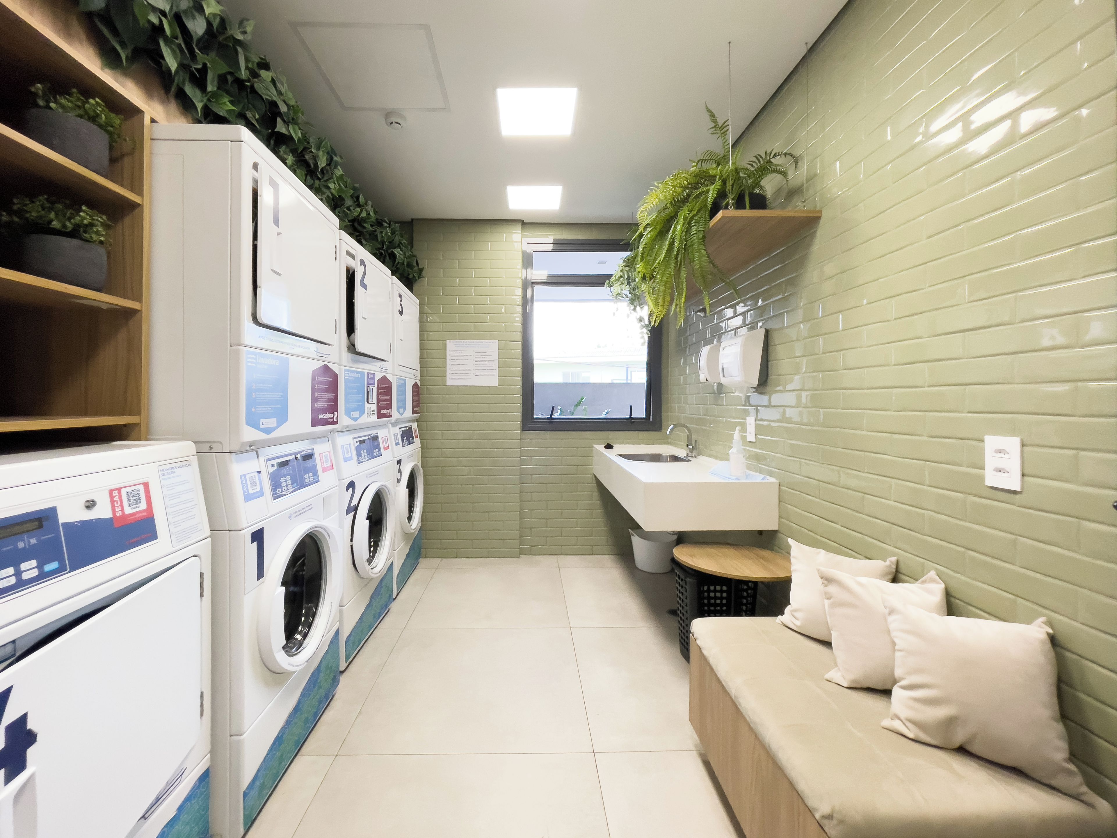 A compact laundry room with stacked washing machines, a sink, and a small seating area.