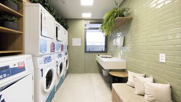 A compact laundry room with stacked washing machines, a sink, and a small seating area.