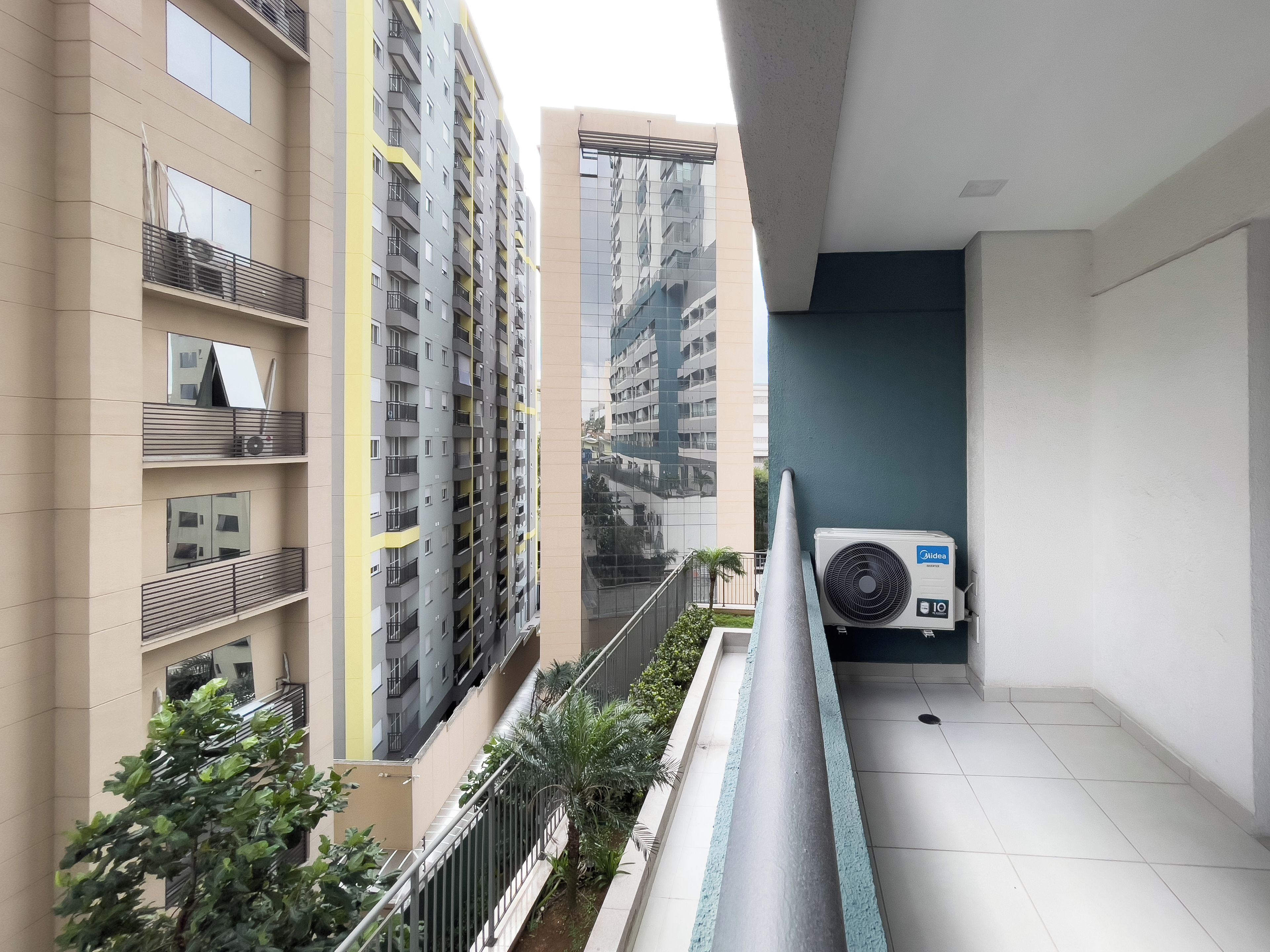 A modern apartment building with balconies, a view of another high-rise, and an air conditioning unit on the balcony.