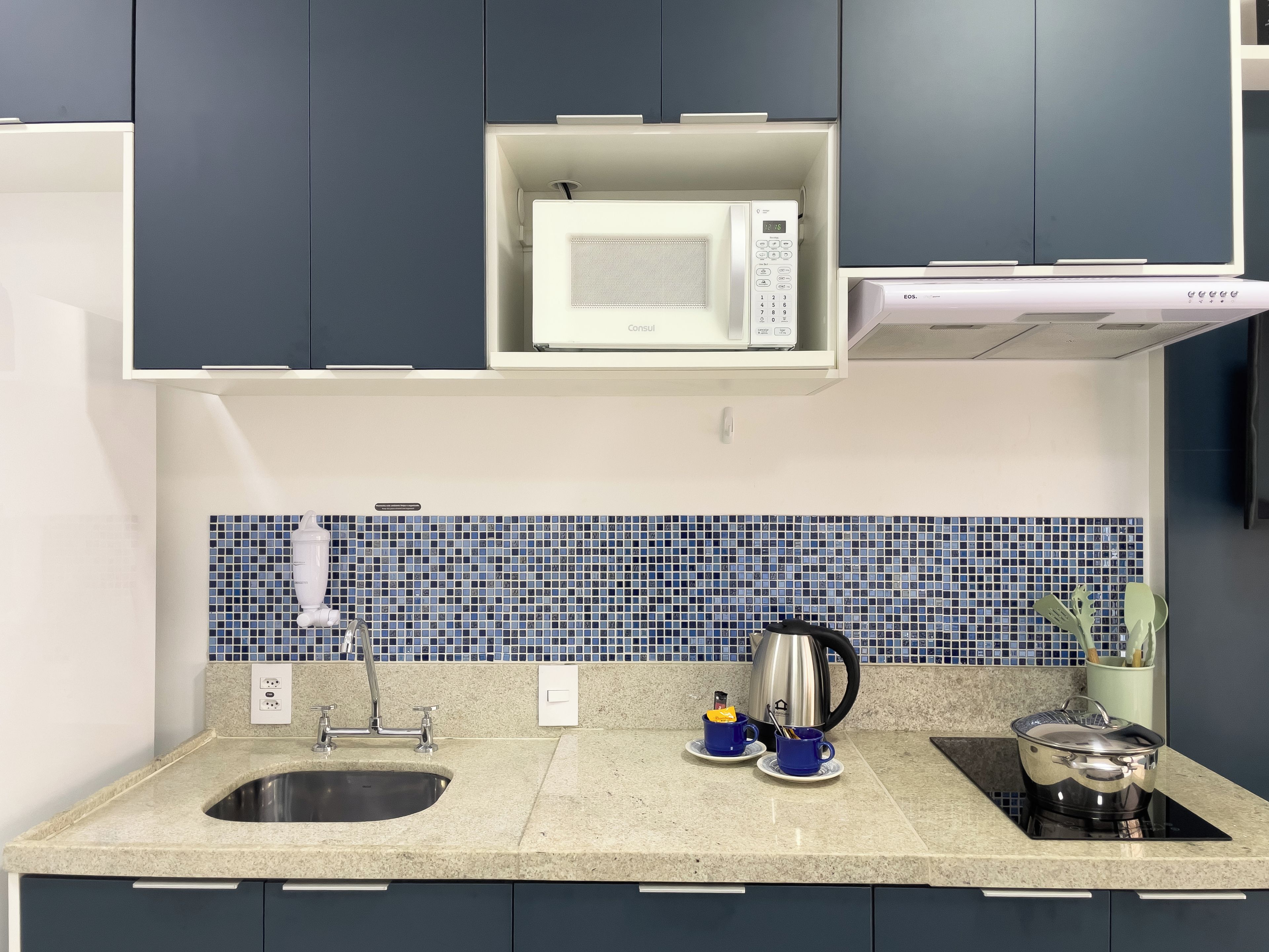 A modern kitchen with a built-in microwave, a kettle, and a stove.