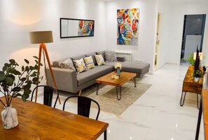 A modern living room with a sofa, coffee table, and dining table. There are paintings on the walls and a floor lamp. - Luxury Sunset House (Marsa)