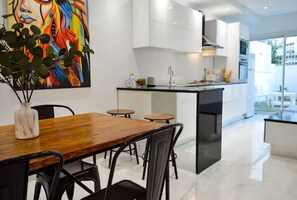 A modern kitchen with white cabinets, a wooden dining table, and a colorful abstract painting. - Luxury Sunset House (Marsa)