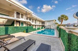 A hotel with a swimming pool, outdoor seating, and a palm tree. - Sandy Serenity at Tenth | Unit 211 (Myrtle Beach)