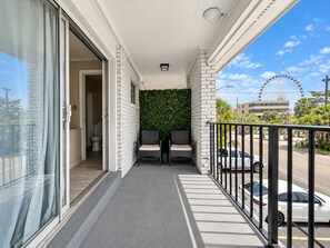 Un balcon d’où l’on peut admirer une grande roue, un immeuble et des voitures garées.