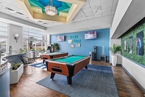 A pool table in a room with a blue wall and a green wall with plants. - Ocean Walk Resort 706 (Daytona Beach)