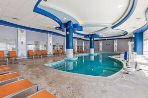An indoor swimming pool with blue and white architectural features, orange chairs, and a clear ceiling. - Ocean Walk Resort 706 (Daytona Beach)