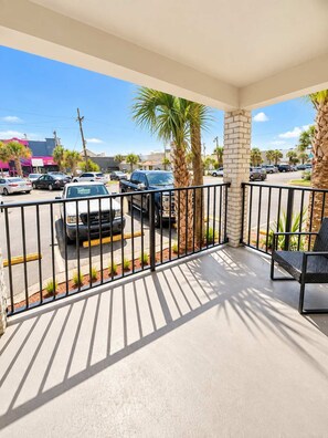 A covered outdoor area with a view of a parking lot and buildings in the background. - Beach Dreams at 300 Tenth | 110 (Myrtle Beach)
