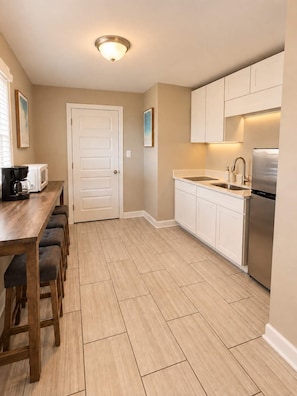 A modern kitchen with a wooden dining table, white cabinets, a stainless steel refrigerator, and a microwave. - Drift Away at 300 Tenth | 105 (Myrtle Beach)