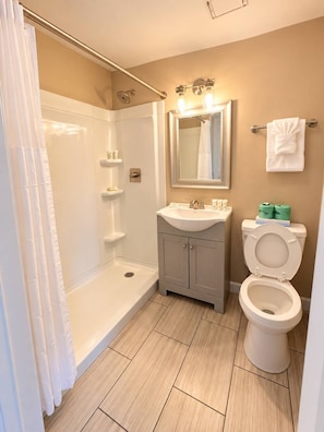 A bathroom with a shower, sink, toilet, and a mirror. - The Salty Getaway at Tenth Ave | 107 (Myrtle Beach)