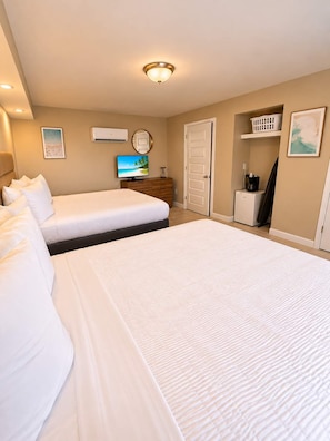 A hotel room with a large bed, a smaller bed, a television, a desk with a coffee maker, and a door leading to a bathroom. - The Salty Getaway at Tenth Ave | 107 (Myrtle Beach)