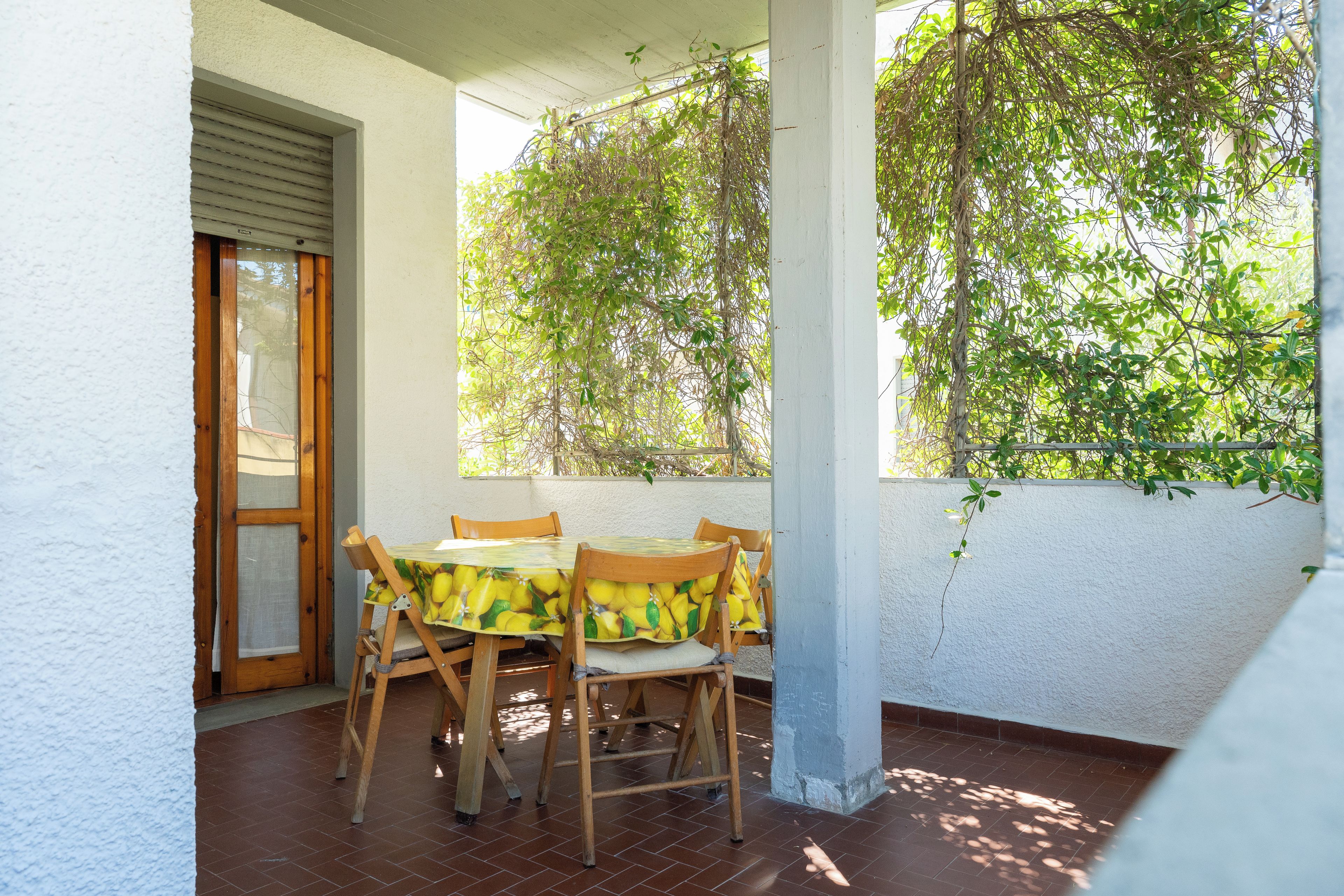 Un patio con una mesa, sillas, una puerta y vista a la vegetación.