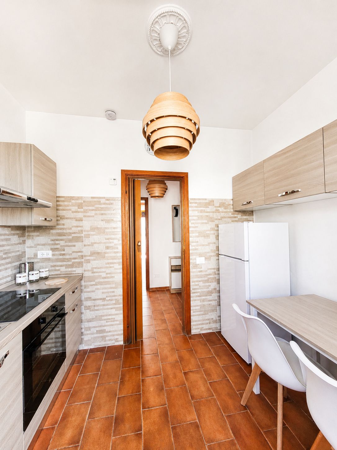 Una cucina moderna con isola centrale, mobili in legno, forno integrato e lampadario a sospensione.