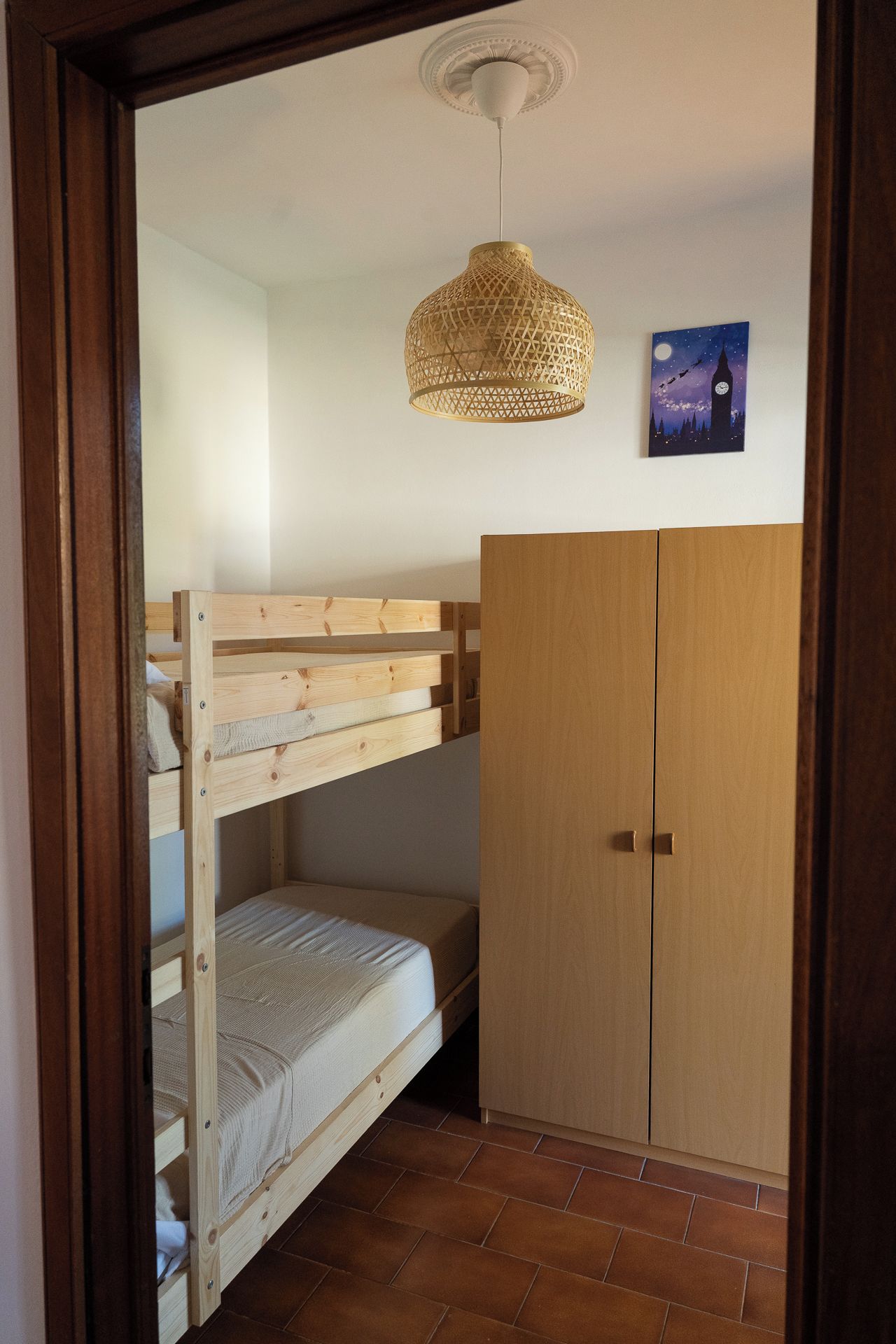 Une chambre avec un lit superposé, une armoire et un luminaire suspendu.