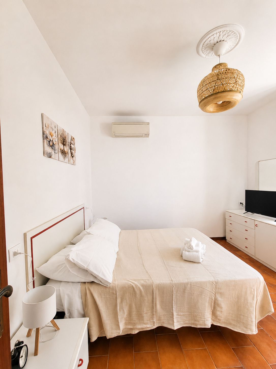 Camera da letto con un letto, comodino, lampada, condizionatore d'aria, un'opera d'arte e televisore su una cassettiera.