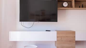 Una sala moderna con un televisor de pantalla plana montado en una pared blanca, un aparador de madera debajo y una pequeña mesa redonda blanca con patas de madera.