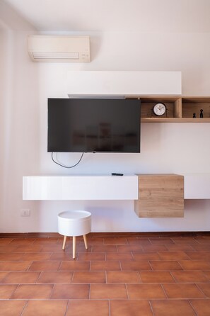 A modern living room with a flat-screen TV mounted on a white wall, a wooden sideboard below, and a small round white table with wooden legs.