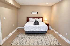 A hotel room with a bed, a bedside lamp, a rug, and a framed picture on the wall. - Lake Ontario Waterfront Retreat | Private Dock (Pickering)