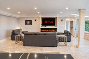Un salon moderne doté d’une cheminée, d’un grand téléviseur à écran plat et d’un espace détente avec des canapés et une table basse.