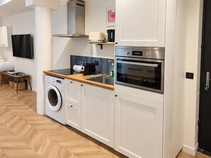 A modern kitchen with a washing machine, oven, and a flat-screen TV mounted on the wall. - Central Paris – A modern and elegant flat (Paris)