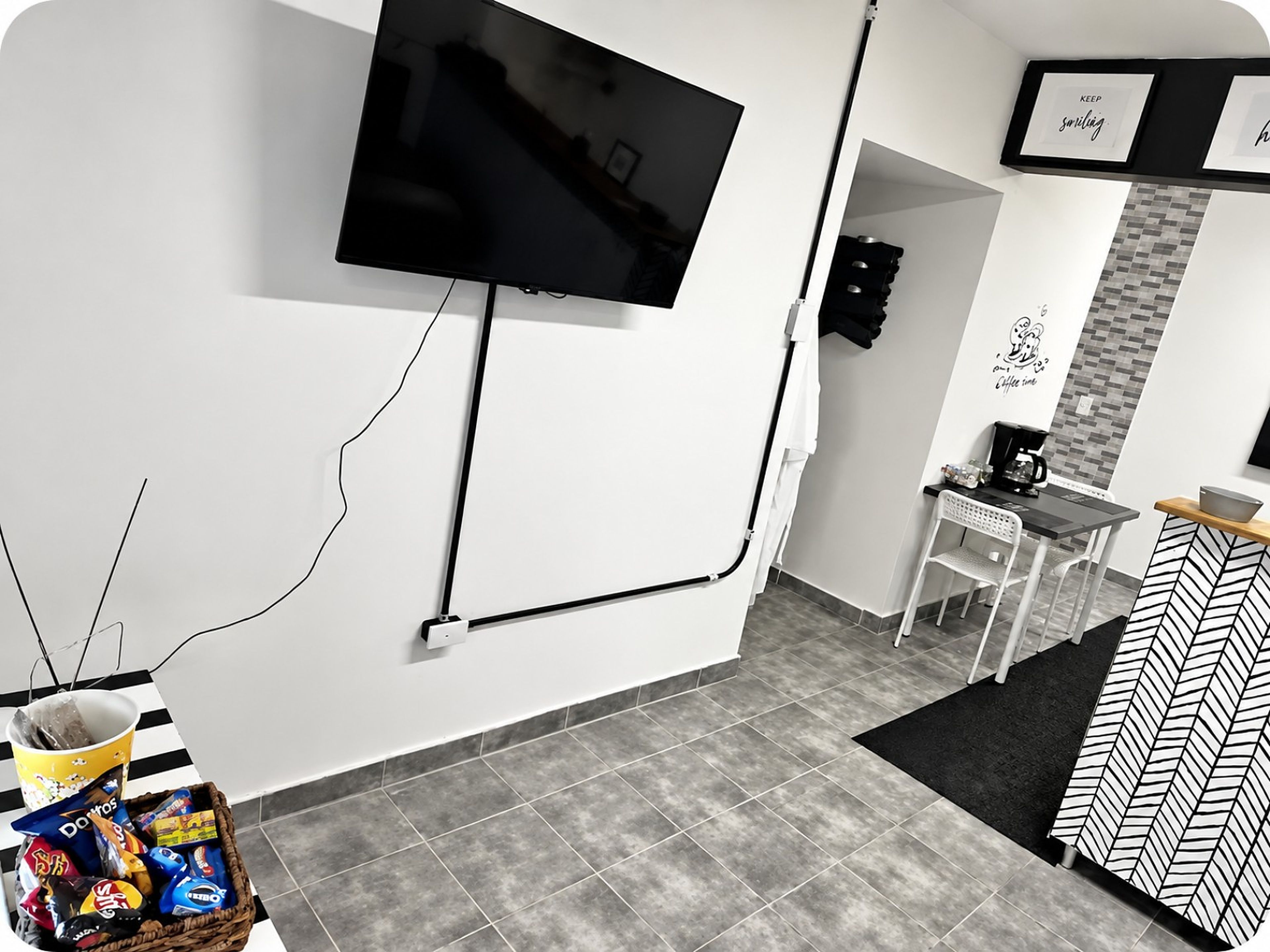 A modern hotel room with a flat-screen TV mounted on the wall, a small dining area with a table and chairs, and a decorative wall with a coffee-themed artwork.