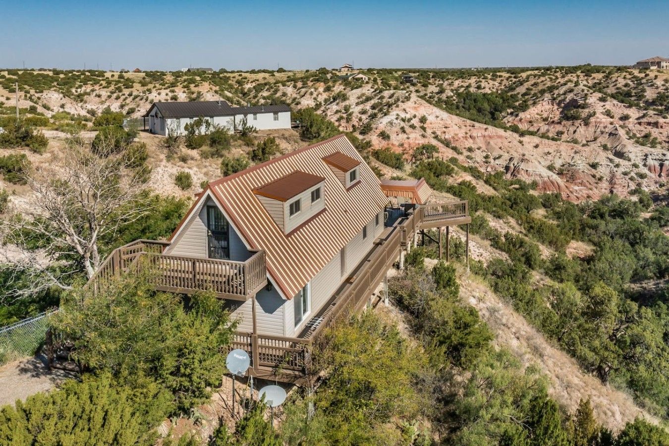 Une maison à deux étages avec une terrasse, entourée de végétation désertique et de collines.