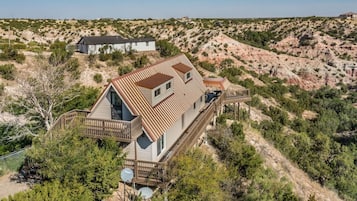 Une maison à deux étages avec une terrasse, entourée de végétation désertique et de collines.