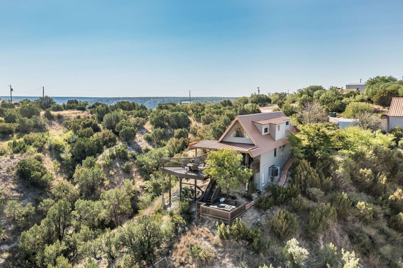 A house with a deck, surrounded by dense vegetation and a clear sky.