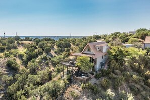 A house with a deck, surrounded by dense vegetation and a clear sky.
