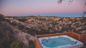 A hot tub on a wooden deck overlooking a hilly landscape.