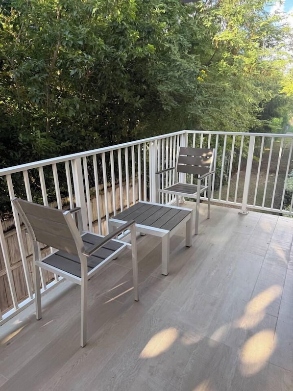Une terrasse dotée d’une balustrade blanche, de deux chaises en bois et d’une table.