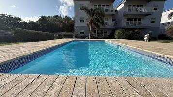 A rectangular swimming pool with clear blue water, surrounded by a wooden deck.