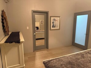 A room with a wooden floor, a white cabinet with a dark cloth, a framed picture on the wall, and a door leading to another room. - Luxurious Beach Front Villa Pool-Gym-AC Sleeps 5! (Turtle Bay)